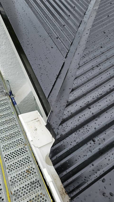 Flashing junction on a newly installed long-run steel roof, photographed where it terminates over the spouting.