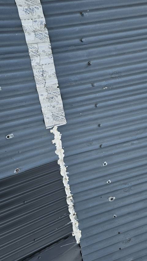 Building tape and a rough bead of sealant run down a sheet lap at the change of pitch, from earlier attempts to stop a leak.