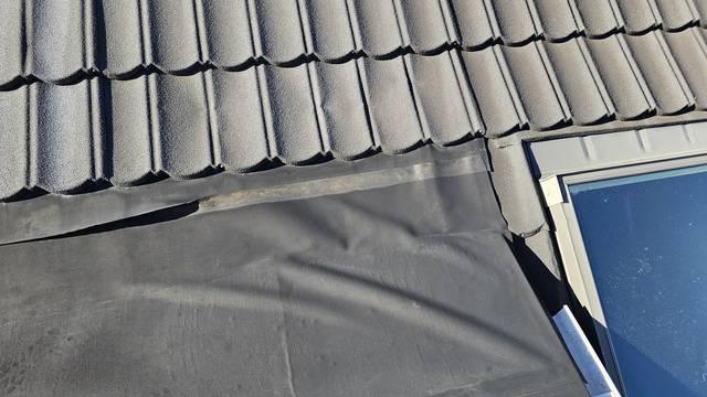 The edge of this Butynol section has pulled away where it meets the pressed metal tiles, leaving the sheet loose and wrinkled with the timber beneath exposed.