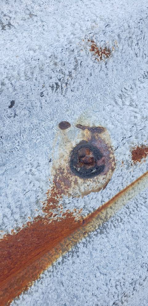 A fixing where the lead head has gone, leaving the nail head bare and rusting into the weathered sheet around it.