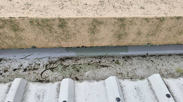 The liquid-applied coating in this internal gutter is delaminating, with patches flaking away to expose the earlier layers beneath.