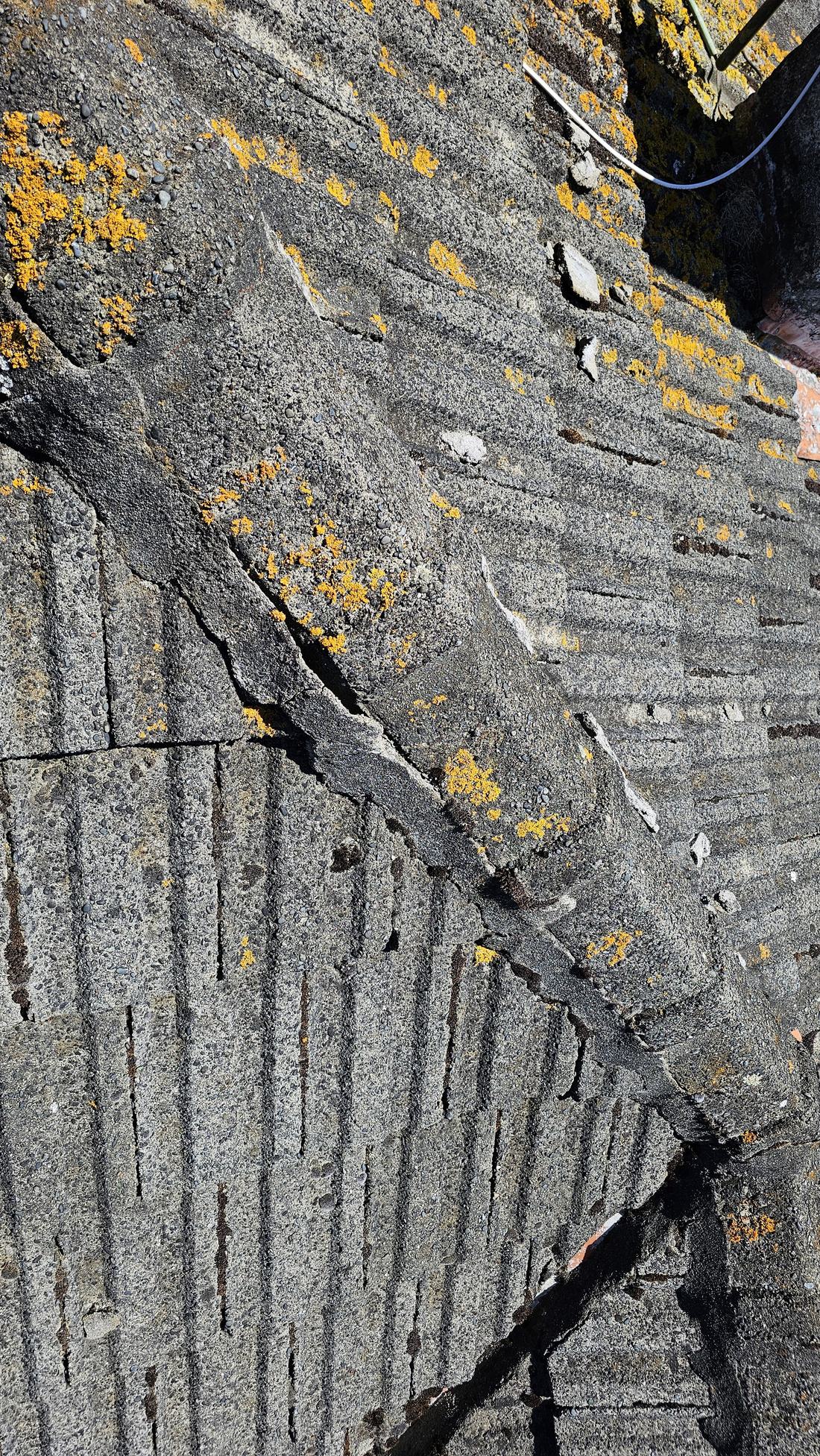 Cracked and crumbling mortar pointing along the hip of a concrete tile roof