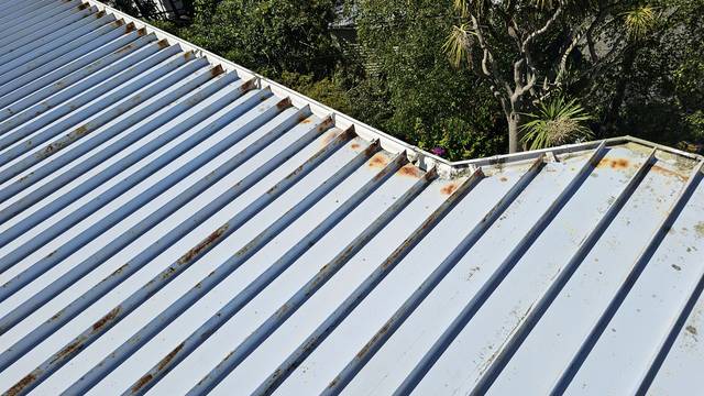 Rust spotting along the rib edges of steel tray sheets, heaviest where the two roof planes meet.