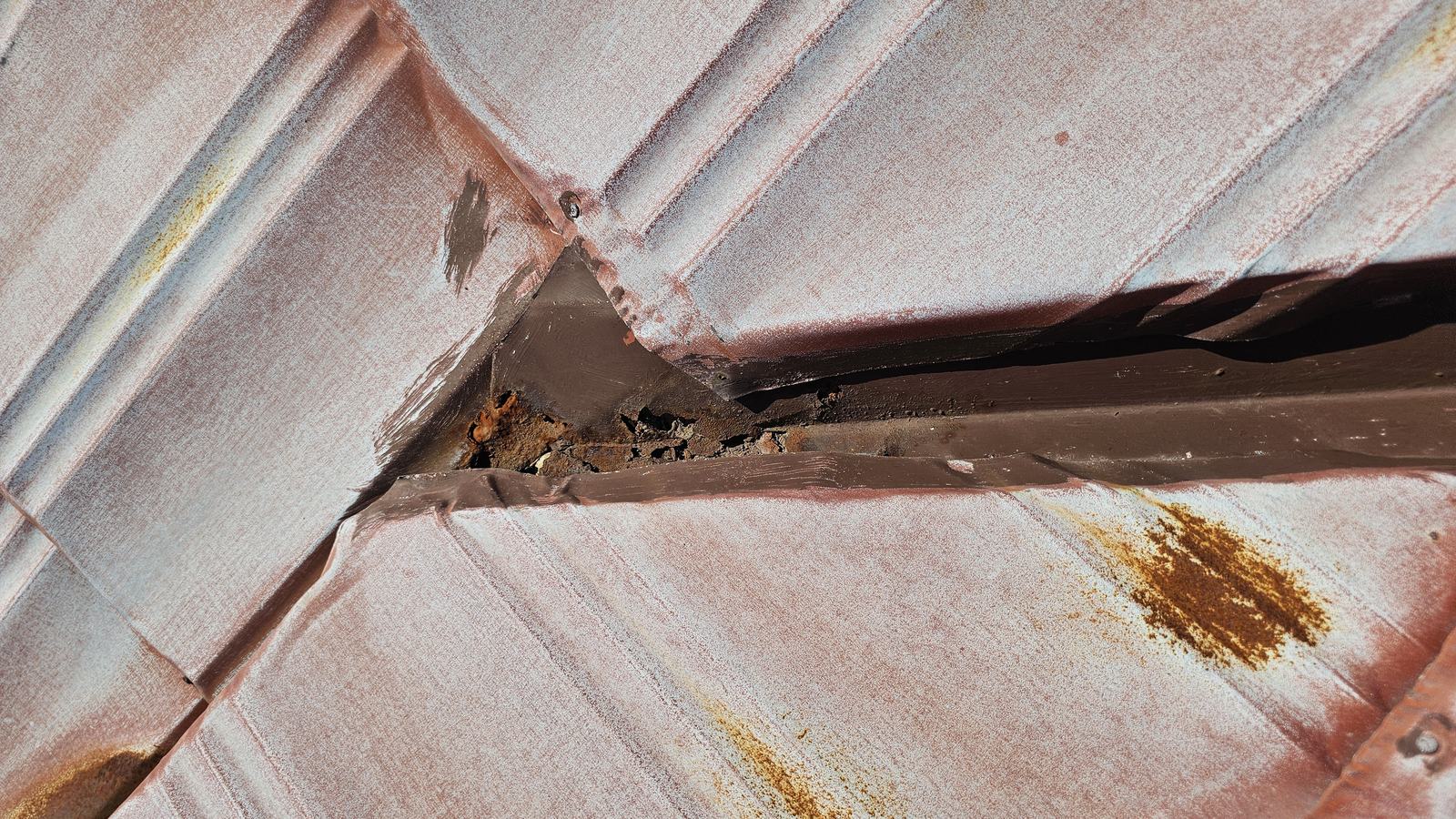 Heavy rust holes through the valley junction of a pressed-metal tile roof, with old sealant around it