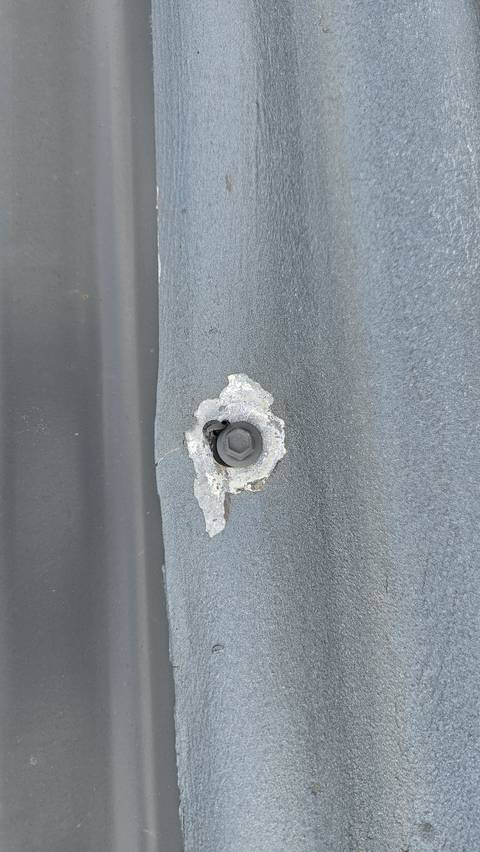Screw fixing on a corrugated iron roof driven in overtight, dishing the sheet and breaking up the coating around it, photographed while the works were still under way.