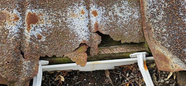 This decramastic tile has rusted right through at the gutter line, with holes opening up and the fascia board visible underneath.